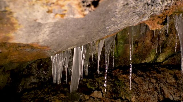 Slow motion close-up of frozen icicle formations hanging from a rocky roof inside a dark underground lava wind cave near Mount Fuji Aokigahara Forest in Minamitsuru District Japan Asia tourism nature