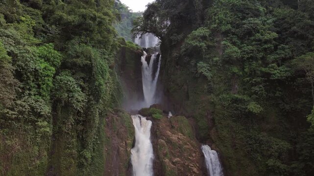 Aerial view of Curug Klenting Kuning waterfall cascading down rocky cliffs surrounded by lush tropical greenery in Kecamatan Limbangan, Central Java, Indonesia.