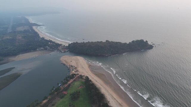 Wide cinematic aerial of Gokarna highlighting layered coastlines, sandy stretches, and textured ocean waves surrounding a dense tropical peninsula fading into the distant horizon.