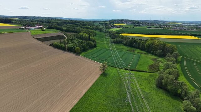 Drone shot flying over agricultural fields, green meadows, and high-voltage power lines in spring