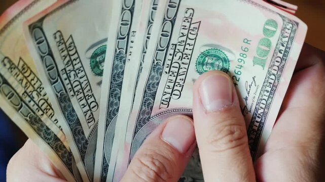 Hands count cash in a close-up shot, revealing crisp 100 dollar bills with dynamic motion, showcasing financial transaction and wealth concept.
