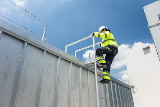 Female engineer climbing a metal ladder for technical installation at construction site, Professional maintenance worker in hard hat and safety gear ascending to inspect HVAC systems