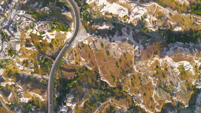 Uchisar, Nevsehir, Turkey. Overhead aerial view of Cappadocia's eroded volcanic tuff plateau, where winding roads cut geometric patterns through golden-brown terrain and pale hoodoo formations. Aeria