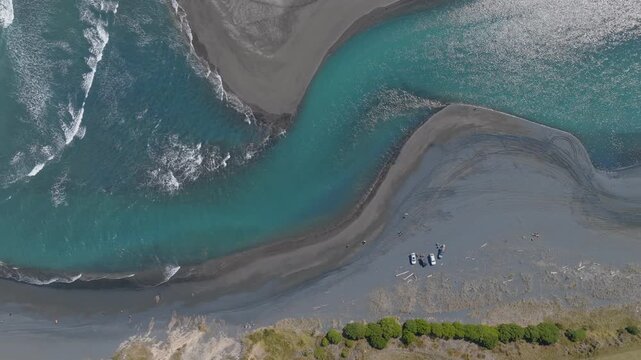 Aerial view of people and vehicles on the beach at the river mouth, in Marokopa, West Coast, New Zealand. Turquoise water meets the ocean.