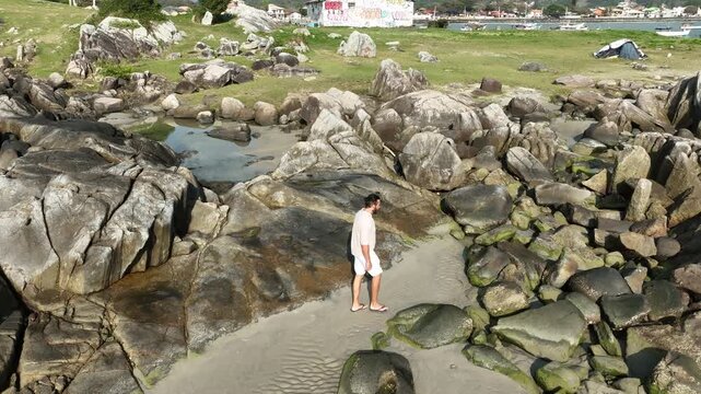 Ponta das Campanhas, Armacao in Florianopolis. A man walks across the island among the rocks. Aerial view.