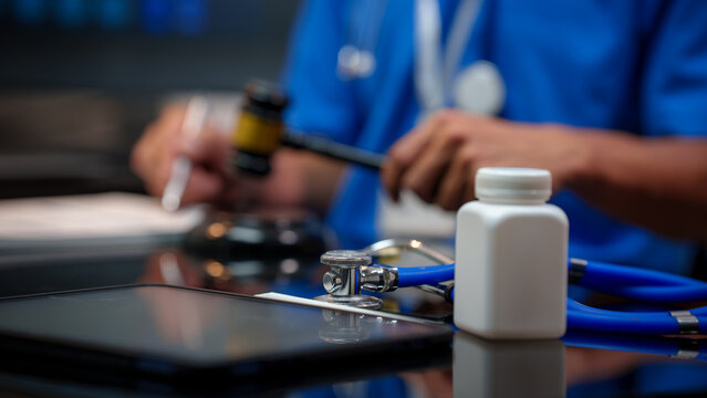 Doctor at desk with stethoscope, medicine bottle, and tablet; gavel in hand suggests healthcare law or medical regulation concept.