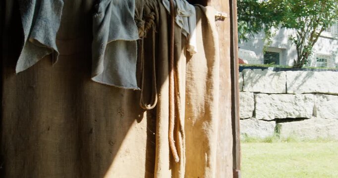 The camera pans left from a bright doorway overlooking a stone wall into the rustic interior of a shed, revealing a large, dense stack of seasoned firewood logs piled against a wooden wall.