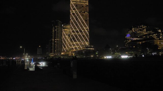 Tilt up night shot of illuminated ITC Ratnadipa Twin Towers rising over Colombo skyline, with glowing diagonal facade lights, city promenade and dark urban sky.