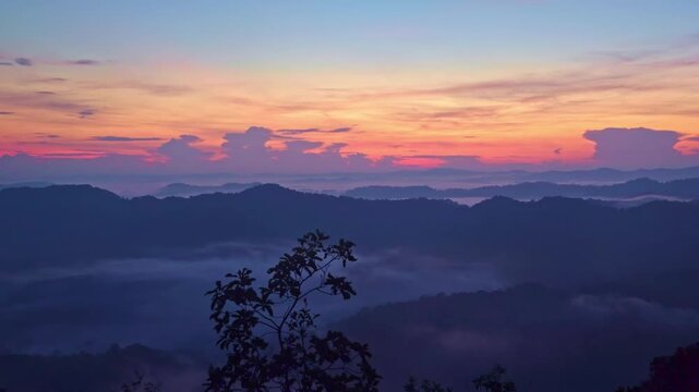 Dawn view from Gunung Fakir Terbang peak. Layered mountain silhouettes emerge from a dense sea of clouds under a vibrant orange and purple sunrise sky in a tropical highland region.