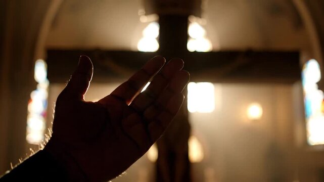 Dramatic silhouette of a faithful open hand raised in divine worship towards a crucifix within a dimly lit cathedral sanctuary, soft atmospheric lighting enhancing the spiritual moment.