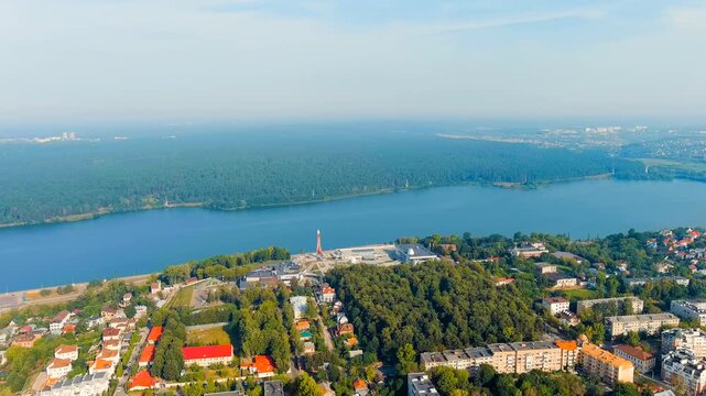 Kaluga, Russia. Yachenskoye Reservoir, panoramic Drone footage over blue water and mixed urban skyline with red-and-white telecommunications tower rising above dense green forest under clear summer s
