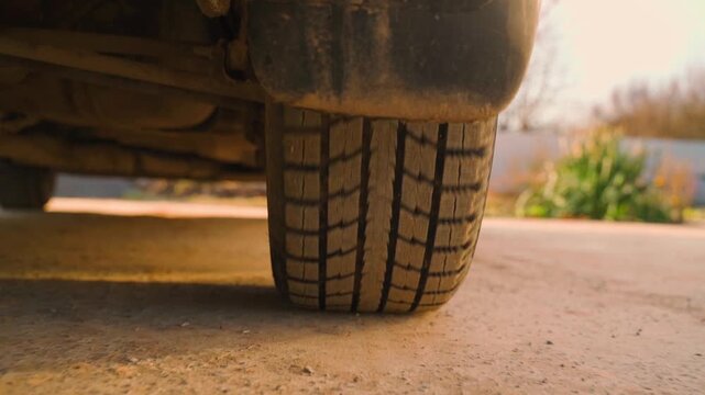 Dirty car tire close up with worn tread on dusty road in countryside