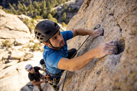 Man climbing rock face with partner
