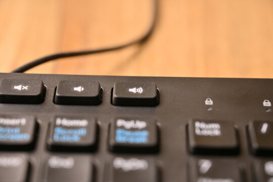 Angled Top View Macro Close-Up Black Computer Keyboard Highlighting Increase Volume Key on Blurred Tech Background
