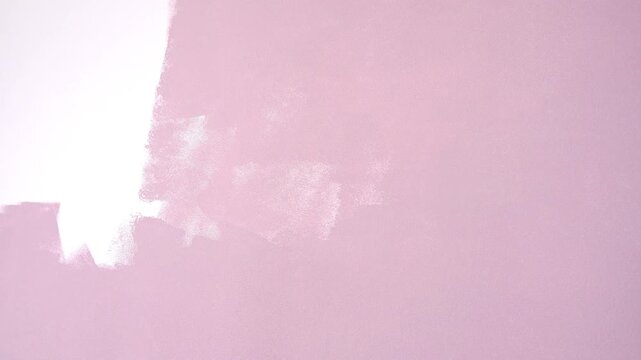 A builder paints a wall pink, apartment construction and renovation, painting walls with a roller