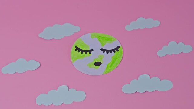Paper Cutout Of Sleeping Earth Planet With Closed Eyes Surrounded Clouds On Pink Background