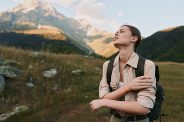Obraz premium A woman outdoors with a backpack stands among mountains, eyes closed, face lifted to the sun, embodying freedom, resilience, and personal discovery.