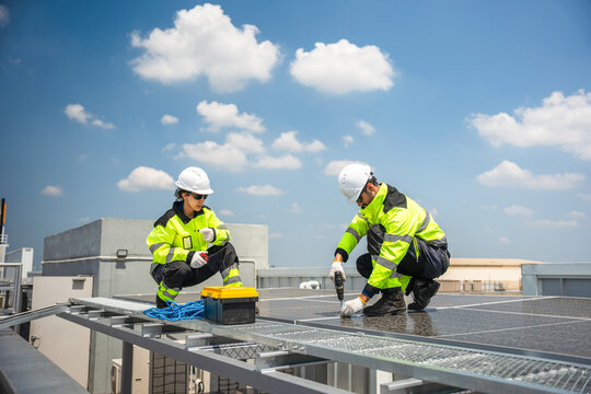 Engineers installing solar panels on rooftop with electric drill, Technicians in reflective jackets maintaining solar energy system, Team of workers installing photovoltaic panels on building roof