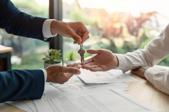 a real estate agent is handing over keys to a customer, illustrating a real estate concept with a close-up of hands and documents on a desk