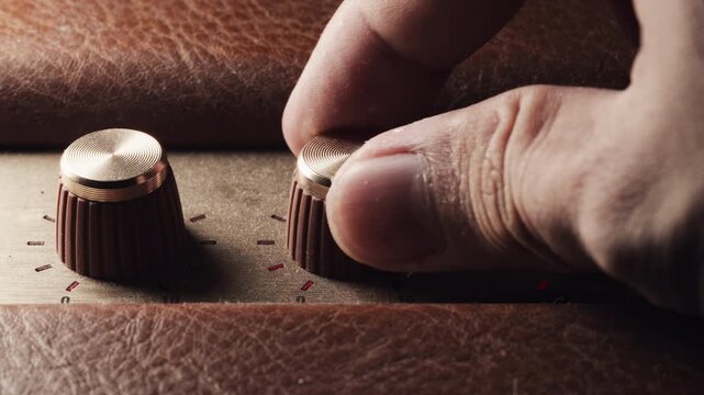 Close up of a hand adjusting gold volume knobs on a vintage leather-wrapped amplifier. A tactile, high-fidelity audio experience highlighting classic analog design and precision sound control