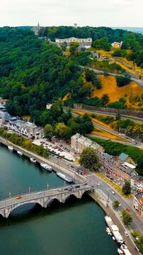 Vertical video. Namur, Belgium. Citadelle de Namur, massive stone fortress crowning a forested hill above the Meuse River, aerial panoramic view on a bright summer day. Drone footage. Rich colors