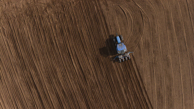 Aerial view of a blue tractor plowing a brown agricultural field with precise parallel lines and curved tire tracks under bright sunlight Lisbon, Lisbon, Portugal.
