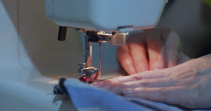 Hands guide blue fabric through a sewing machine, carefully creating neat stitches. The close-up captures the precision and artistry involved in the sewing process. 60 fps 4k footage.