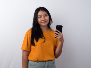 Fototapeta premium Smiling young Asian woman in a yellow shirt is using her smartphone to look at social media, isolated by white background.