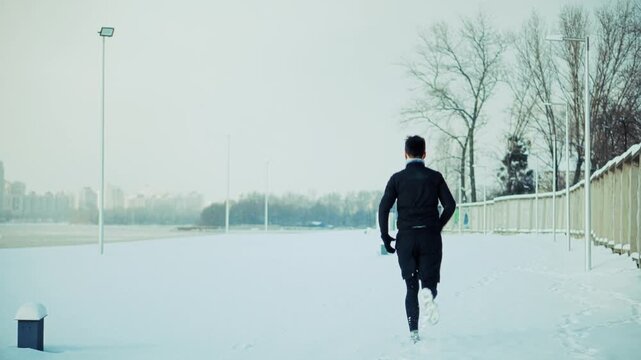 Runner Jogging on Snowy Path in Park. Athlete Training Outdoors during Cold Season. Wellness Activity in Frosty Weather