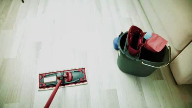 Cleaner Mopping Light Wooden Laminate Floor. Using Microfiber Flat Mop and Plastic Bucket with Water for Wet Cleaning. Sanitary Maintenance and Floor Care in Apartment