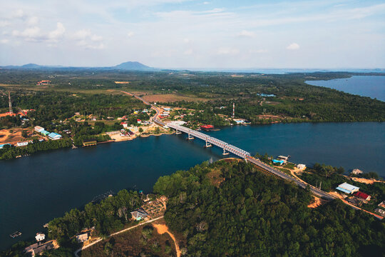 Aerial view of a long bridge spanning across a wide river surrounded by dense tropical forests and small settlements under a clear sky Tanjungpinang, Kepulauan Riau, Indonesia.