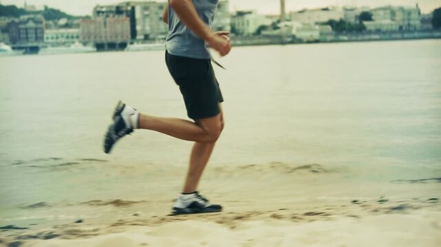 Runner Jogging on Sandy River Beach Embankment against Cityscape Background. Morning Workout and Cardio Exercise