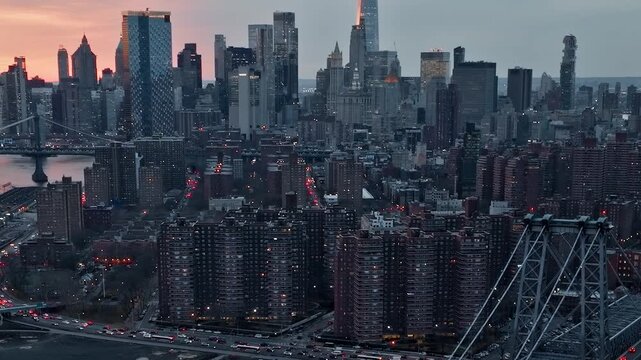 Aerial view of lower Manhattan skyline at dusk with traffic moving on FDR Drive and Williamsburg Bridge.