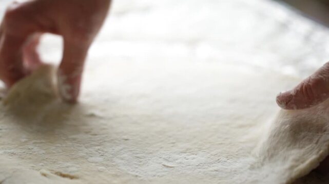 A woman in her kitchen rolls out dough to prepare potato dumplings
