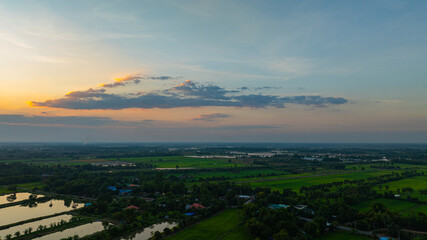 Obraz premium A stunning golden sunset reflecting on a calm lake surrounded by rural greenery and tree silhouettes. The dramatic clouds and warm evening light create a peaceful natural landscape perfect for travel