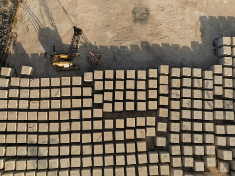Aerial view of large concrete blocks arranged in a grid at an industrial site with a yellow crane casting long shadows Priolo Gargallo, Sicily, Italy.