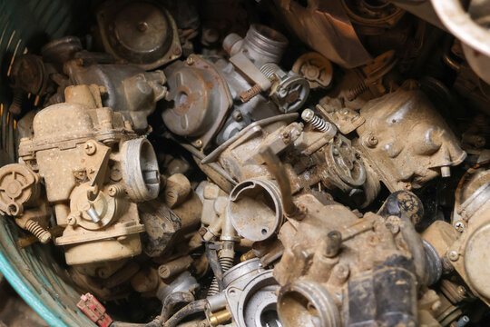 Pile of old rusty metal carburetor engine part scrap junk dirty and neglected feeling forgotten workshop. Close view shows detail of discarded broken component waste ready for recycling process