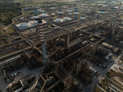 Aerial view of the vast industrial oil refinery complex with storage tanks and tall striped smokestacks under soft daylight in Priolo Gargallo, Sicily, Italy.