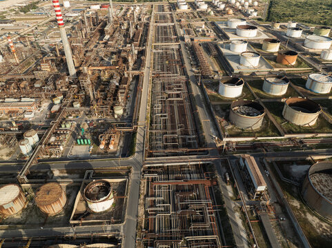 Aerial view of the vast industrial complex and oil refinery featuring storage tanks, intricate piping systems, and tall chimneys under bright daylight in Priolo Gargallo, Sicily, Italy.