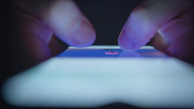 A man is looking at images on his smartphone at night, close-up of his hands, front view