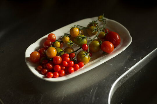 Assorted cherry tomatoes on a vine in a porcelain plate, moody lighting