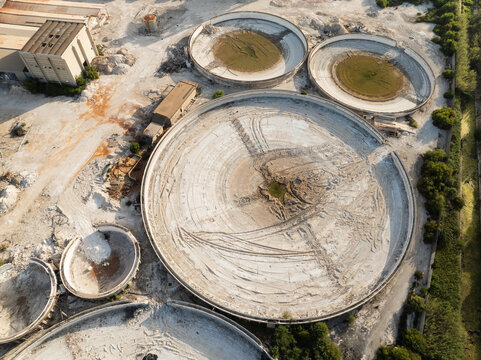 Aerial view of large circular industrial basins and sedimentation tanks at a processing facility surrounded by greenery in Priolo Gargallo, Sicily, Italy.