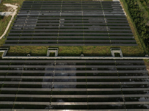 Aerial view of rows of photovoltaic solar panels installed on a green field with industrial infrastructure Priolo Gargallo, Sicily, Italy.