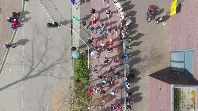 Aerial drone view of people running half marathon race in city, shadows of runners on road racing sport competition, top-down view of athletes and spectators