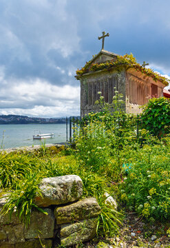 Traditional stone horreo with cross overlooking the sea and a boat in Combarro Galicia, Spain