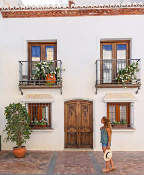 woman standing in front of a traditional white house with wooden door and flower balconies in Andalusia Spain, Malaga