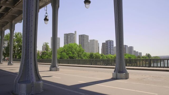 Cinematic view of Bir Hakeim bridge steel columns with Parisian skyline and modern residential buildings in distance.