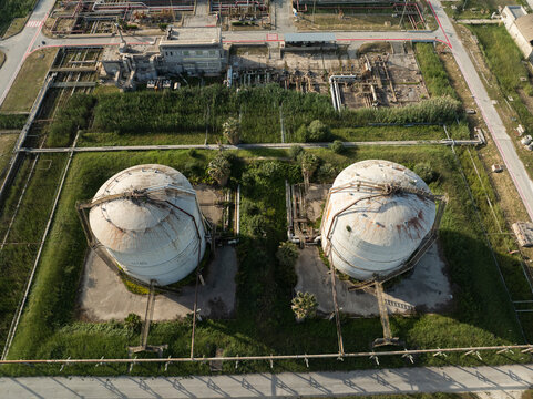 Aerial view of two large spherical industrial storage tanks surrounded by lush greenery and complex piping systems in Priolo Gargallo, Sicily, Italy.