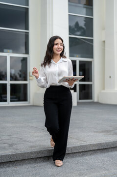 Full body of asian businesswoman holding tablet and pen while standing walking outside the building.
