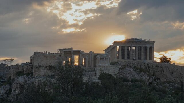 A moody morning timelapse of the Athens Acropolis. The sun breaks through moving clouds, casting shifting light and shadows over the ancient Parthenon and Propylaea ruins at dawn.
